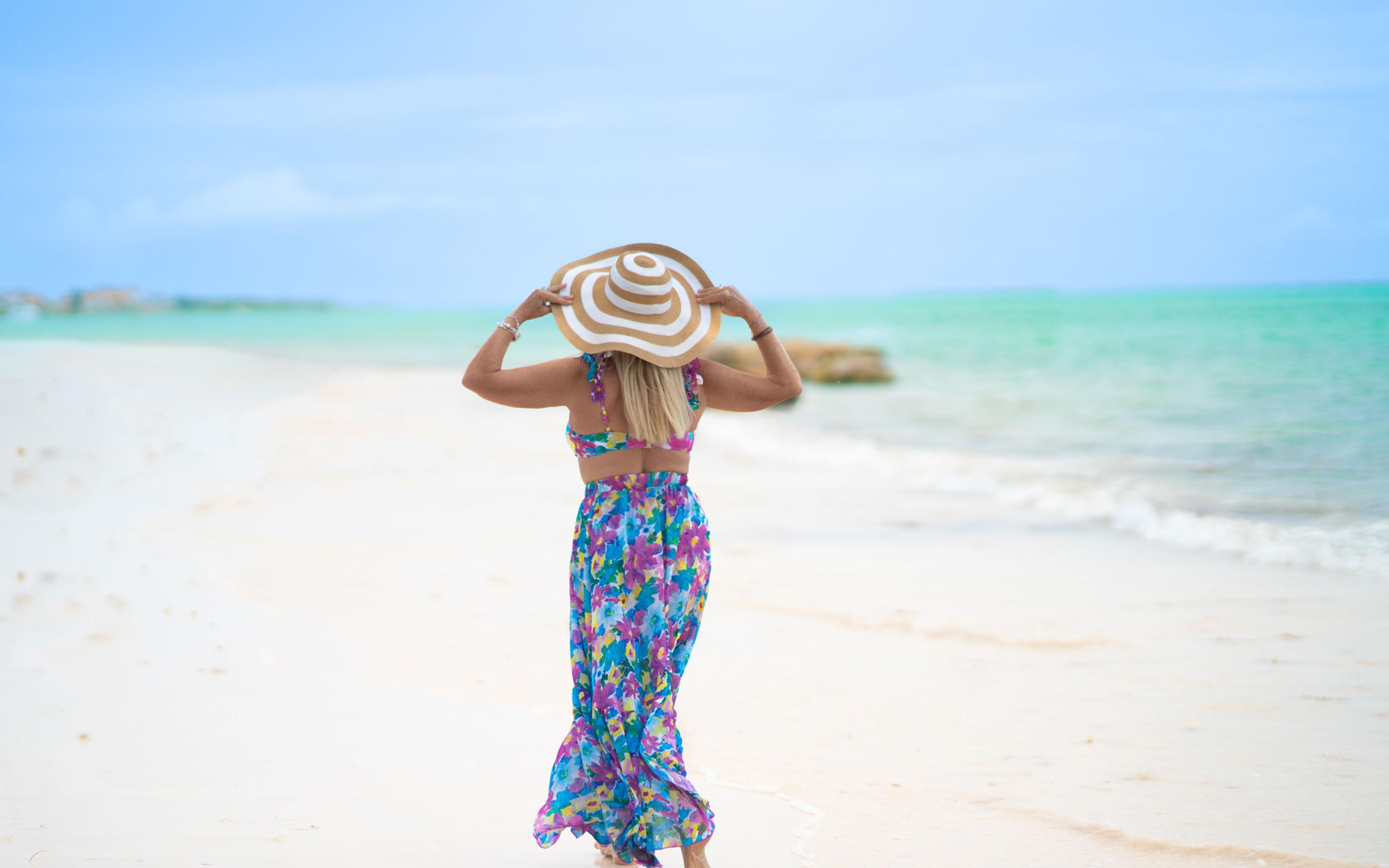 a woman walking on a beach wearing a flower dress